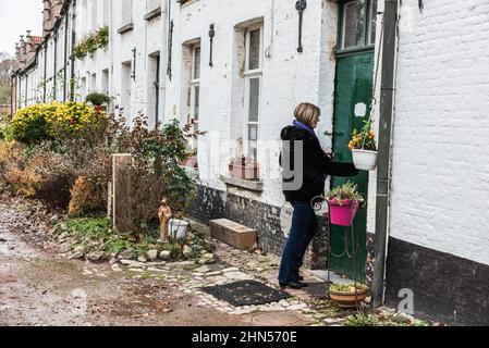 Dendermonde, Flandern / Belgien - 12 08 2018: Junge Frau öffnet die Haustür ihres Hauses im alten Beginenhof Stockfoto