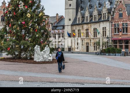 Dendermonde, Ostflandern - Belgien - 12 08 2018: Frau, die über den alten Marktplatz mit mediëval façades und einem geschmückten Weihnachtsbaum spaziert Stockfoto