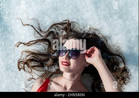 Nahaufnahme einer kaukasischen Frau, die in einer Sonnenbrille auf dem Schnee liegt. Draufsicht. Stockfoto