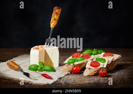 Baguette mit Kirschtomaten, weichem Schafskäse und Basilikum auf schwarzem Hintergrund. Traditionelle italienische Vorspeise oder Snack. Stockfoto