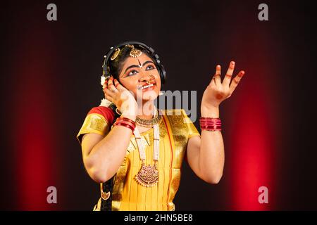 Genießen Sie die indische bharatanatyam-Tänzerin beim Hören eines Lieblingsliedes auf Kopfhörern auf der Bühne - Konzept der Entspannung, klassischer Tänzer und Unterhaltung. Stockfoto