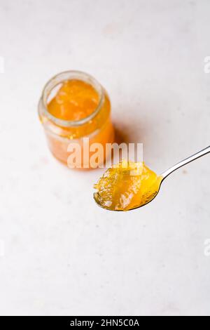 Löffel Obstmarmelade mit einer Flasche im Hintergrund, Nahaufnahme auf einer weißen strukturierten Oberfläche mit Kopierraum, von oben aufgenommen Stockfoto