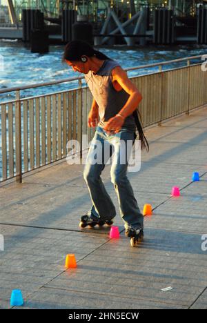 Ein junger Mann übt seine engen Kurven, während er Inline-Skates verwendet und Tassen verwendet, um die Kurven im Battery Park, New York City, zu markieren Stockfoto