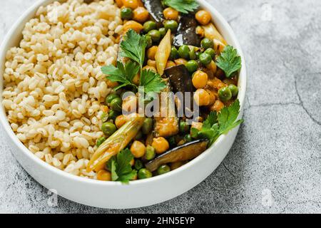 Auberginen Kichererbsen Erbsen vegetarisches veganes, veganes, mit Bulgur in einer Pfanne auf grauem Hintergrund, Draufsicht. Indische Küche. Gesundes Essen. Vegan. Pflanzenbasis. Stockfoto