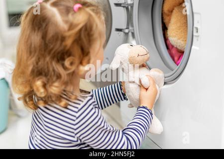 Das Kind beobachtet, wie die Waschmaschine waschen wird. Stockfoto