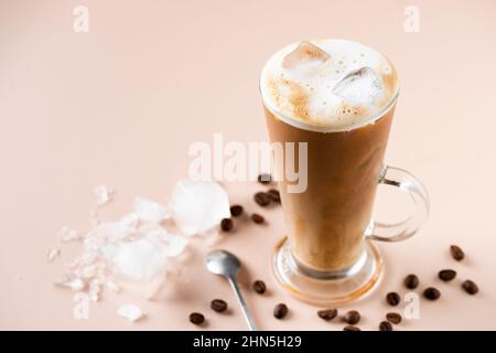 Eiskaffee Latte in einem Glas auf beigem Hintergrund. Erfrischendes kaltes Getränk Stockfoto