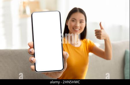 Fröhliche junge asiatische Frau zeigt Smartphone mit leerem Bildschirm Stockfoto