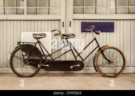 Altes schwarz verwittertes Tandemfahrrad vor einer alten Fabriktür Stockfoto