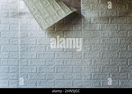 Die Tapete beginnt sich abzulösen. Die Tapete aus alten weißen Ziegeln schälte sich von der Wand im Raum, weil es feucht war oder sich nicht gut klebte. Reparieren Sie A Stockfoto