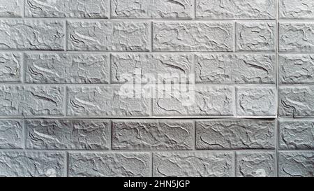 Die Tapete beginnt sich abzulösen. Die Tapete aus alten weißen Ziegeln schälte sich von der Wand im Raum, weil es feucht war oder sich nicht gut klebte. Reparieren Sie A Stockfoto