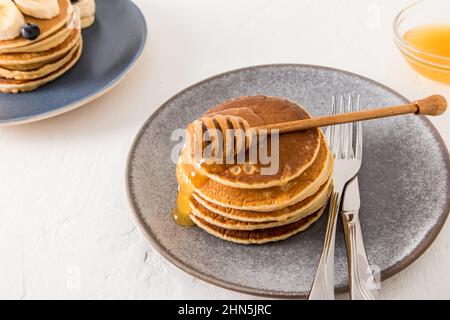 Ein Stapel dicker Pfannkuchen auf einem grauen Teller mit Honig, der durch sie fließt. Das Konzept eines gesunden leckeren Snacks Stockfoto