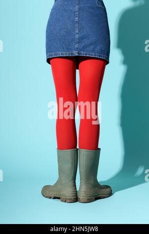 Rückansicht der Ernte unkenntlich weiblich trägt Denim Rock mit leuchtend roten Strumpfhosen und grünen Gummistiefel im Studio stehen Stockfoto