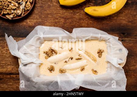 Ungekochte Teig Bananenbrot in der Form. Kochen. Holzhintergrund. Blick von oben. Süßes, vegetarisches Essen. Stockfoto