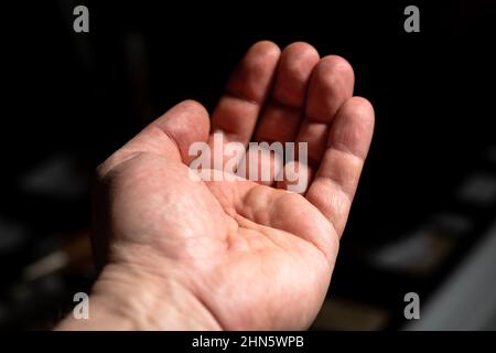 Leere männliche Hand. Ausgestreckte Hand eines Mannes auf dunklem Hintergrund. Stockfoto