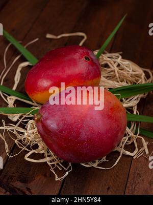 Mangofrüchte mit Blättern auf Stroh und Holztisch Stockfoto