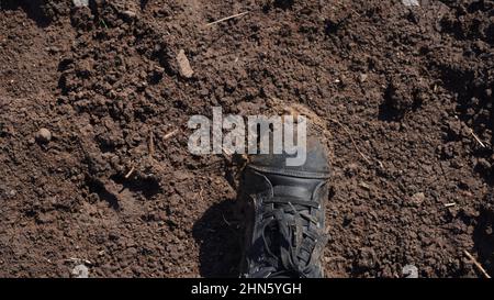 Frauen Stiefel im Schlamm, Detail von schmutzigen Stiefeln und schlammig, zu Fuß. Top down schmutzige schwarz geschnürte Stiefel Frau in blauen Jeans. Stockfoto