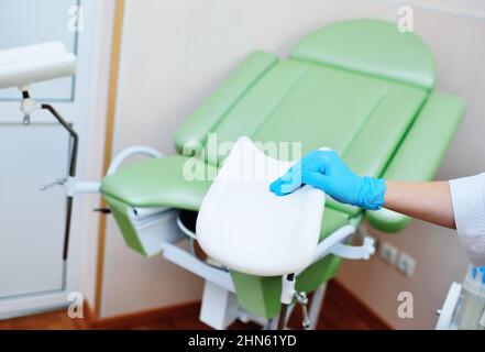 Der Gynäkologe, der Gummihandschuhe anzieht, bereitet sich auf die Untersuchung vor dem Hintergrund des gynäkologischen Stuhls vor. Stockfoto