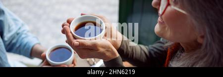 Lächelnde reife Frau mit Freund halten Tassen Tee an einem kleinen Tisch im Café Stockfoto