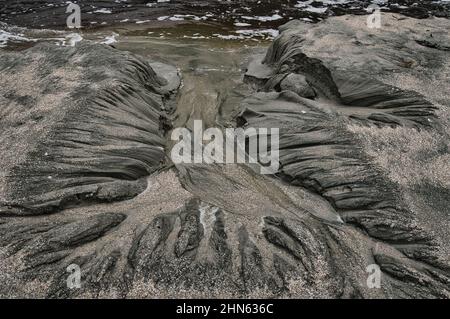 Abstrakte Flussmuster in nassem schwarzen Sand an einem Strand in Neuseeland Stockfoto