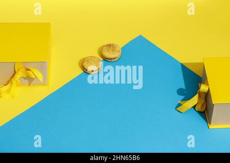 Gelbe Geschenkbox mit Schleife und zwei französischen Makronen auf gelbem und blauem Hintergrund. Gruß zum Internationalen Frauentag am 8. März, mot Stockfoto