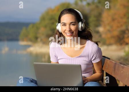 Vorderansicht Porträt einer glücklichen Frau mit Laptop und Headset sieht Sie in der Natur Stockfoto