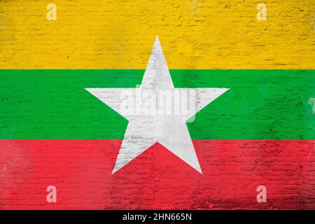 Vollformatfoto einer verwitterten Flagge von Myanmar, gemalt auf einer verputzten Ziegelwand. Stockfoto