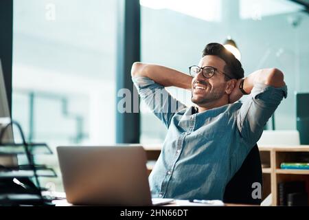 Die Deadline zu schlagen, wie der Herr, der er ist. Aufnahme eines jungen Geschäftsmannes, der in einem modernen Büro an seinem Schreibtisch eine Pause einlegte. Stockfoto