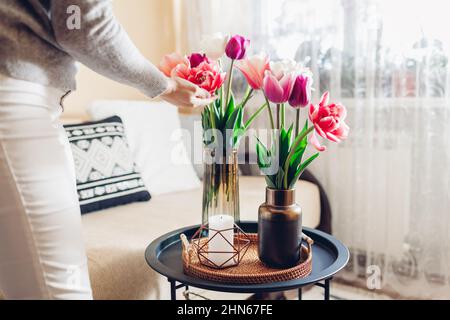 Frau genießt Tulpen Blumen in Vasen auf Tisch mit Tablett und Kerze gesetzt. Gemütliches Interieur und Frühlingsdekor zu Hause Stockfoto