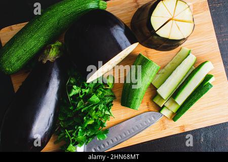 Auberginen und Zucchini in Keile schneiden: Auberginen und Zucchini-Keile auf einem Schneidebrett aus Bambusholz Stockfoto