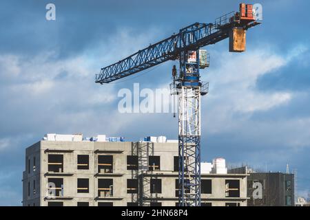 Baustelle mit Kran, Neubauten oder im Bau befindliche Häuser mit bewölktem Himmel im Hintergrund Stockfoto