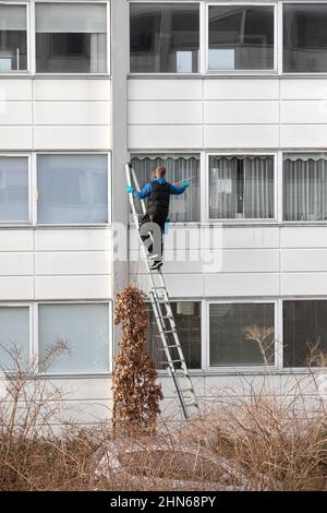 Arbeiter auf einer Leiter, der die Außenfenster des Wohngebäudes reinigte Stockfoto