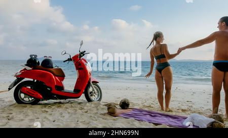 Motorroller Road Trip. Schönes Paar auf rotem Motorrad in weißen Kleidern am Sandstrand. Hochzeit gerade verheiratete Menschen, die in der Nähe von tropischen Palmen, Meer. Flitterwochen am Meer. Asien Thailand. Motorradmiete. Stockfoto