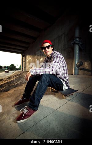 Skateboarder sitzt unter der Überführung an Bord Stockfoto