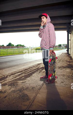 Skateboarder unter Überführung steht mit Brett Stockfoto