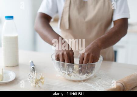 Eine tausendjährige afroamerikanische Frau in der Schürze, die Teig auf dem Tisch in der Küche macht, aus nächster Nähe Stockfoto