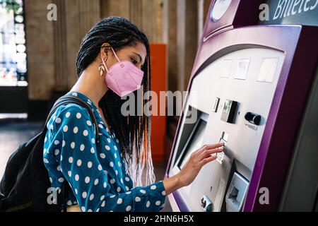 Hispanische Frau in medizinischer Maske Kauf Ticket im Bahnhof Stockfoto
