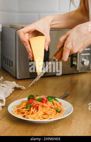 Nahaufnahme des Handreibeparmesans auf einer Reibe über einem Teller Pasta in der Küche Stockfoto