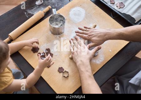 Vater rollt Plätzchenteig aus, Tochter hält Schimmel zum Schnitzen Stockfoto