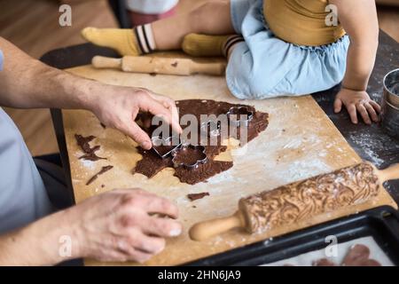 Papa schneidet Schokoladenkekse mit einer Form aus Stockfoto