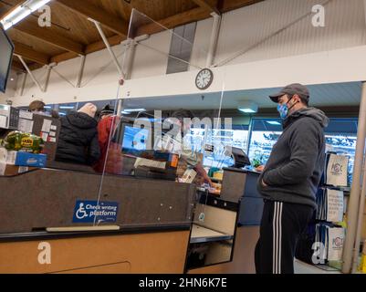 Kirkland, WA USA - ca. Dezember 2021: Ansicht eines männlichen Kassierers hinter einem Plexiglas-Trennwand an einem Kassenschalter in einem PCC-Lebensmittelgeschäft während des Cor Stockfoto