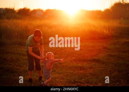 Junge spielt mit seinem Bruder auf dem Gras bei Sonnenuntergang Stockfoto