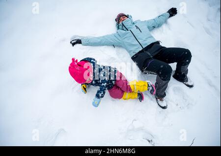 Mutter und Tochter machen gemeinsam Schneeengel. Stockfoto