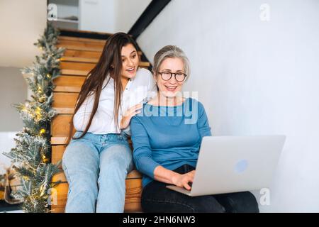 Mutter und Tochter sitzen auf der Treppe und schauen sich etwas auf dem Laptop an Stockfoto