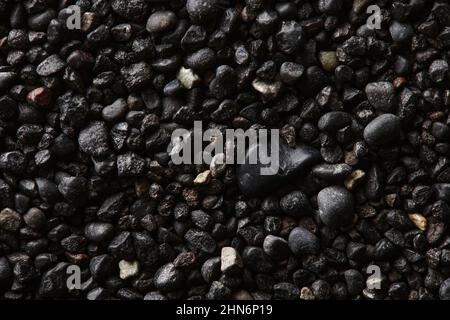Textur aus schwarzem vulkanischem Sand als Hintergrund. Makrofotografie mit schwarzem Sand am Strand. Nahaufnahme der vulkanischen Sandoberfläche. Isländisches Schwarzsandmakro Stockfoto