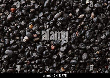 Textur aus schwarzem vulkanischem Sand als Hintergrund. Makrofotografie mit schwarzem Sand am Strand. Nahaufnahme der vulkanischen Sandoberfläche. Isländisches Schwarzsandmakro Stockfoto