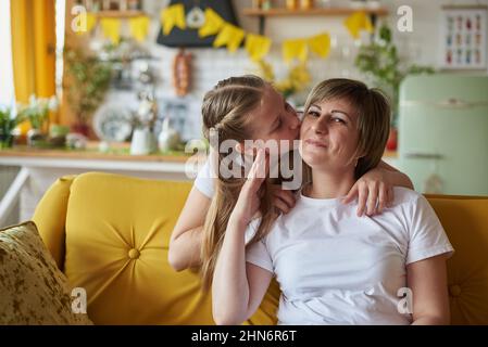 Tochter küsst Mutter sitzt auf der Couch in der Küche. Stockfoto