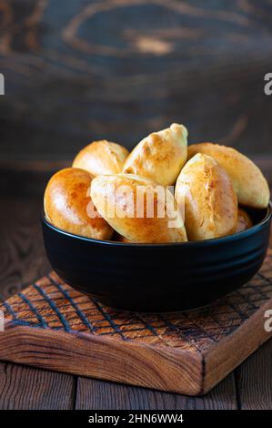 Gefüllte Kartoffelhandgebäck in einer schwarzen Schüssel auf einem Holzbrett. Stockfoto