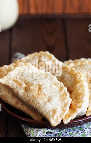 Frisch gebratene Empanadas oder Chebureki mit Fleisch auf einem Teller serviert. Holzhintergrund. Nahaufnahme. Stockfoto