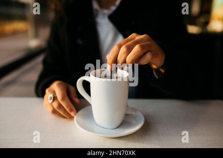 Nahaufnahme der Hände einer jungen Frau mit einem weißen Becher, der Tee in einem Coffeeshop zubereitet Stockfoto