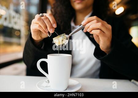 Nahaufnahme der Hände einer jungen Frau mit einem weißen Becher, der Tee in einem Coffeeshop zubereitet Stockfoto